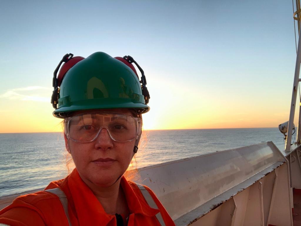 Lílian Pereira no campo, com EPI (capacete), ao pôr do sol